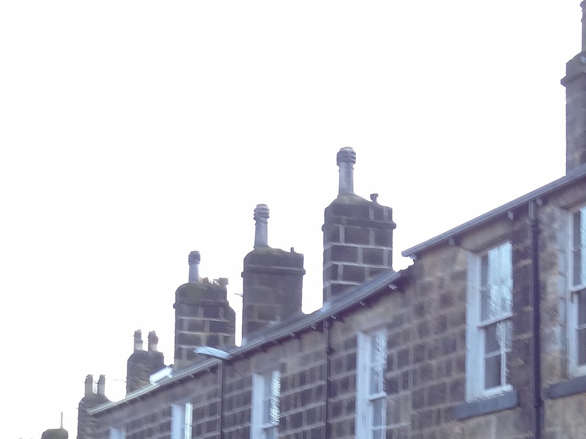 Gritstone chimney stacks and clay pots standing above the roof of a stone terrace