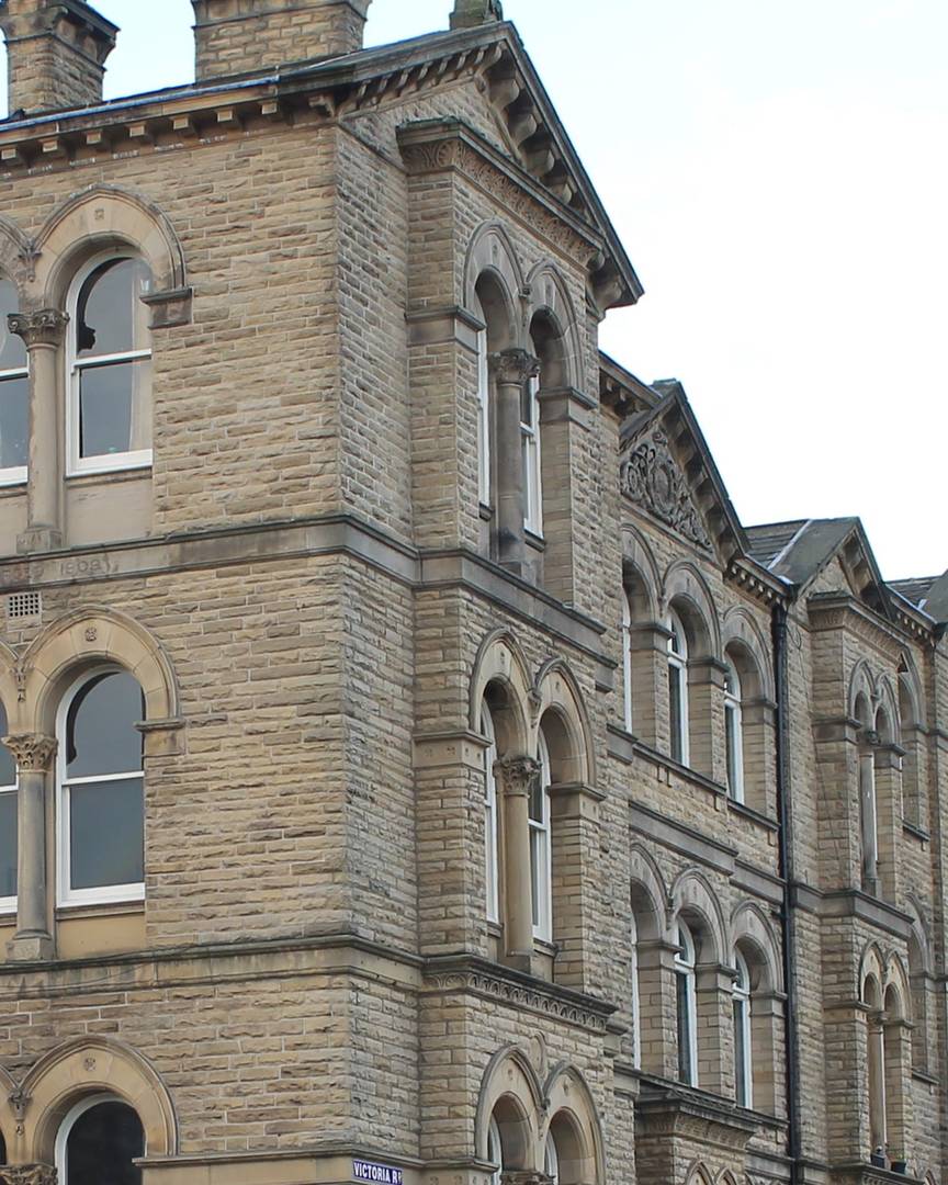Stone mill-town elevation with arched windows under a pitched roof and chimney stacks